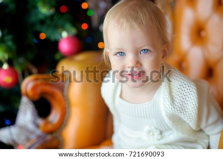 happy little girl with surprise looks at the camera, in the background festive Christmas tree