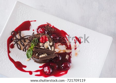 Chocolate cake on white plate with jam, decorated by cherry, almond and mint. Delicious dessert serving in restaurant, close up picture with free space