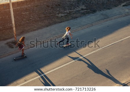 Two young women riding skateboard on the road.