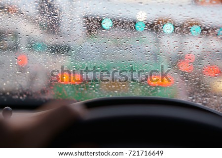people driving car and water droplet on car mirror or windshield with rain storm and traffic jam on expressway road with red light at behind the car and green traffic light