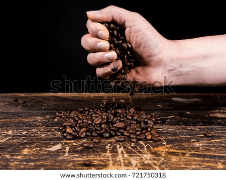 Womens hand with coffee beans with black background over wooden table