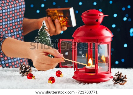 Christmas picture. Bright festive decorations. A girl's hand lights on a Christmas evening a red lantern on a white snow match on a bright blue background with a bokeh. On the snow cones and balls 