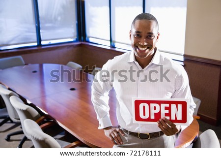African American office worker holding open sign in empty boardroom