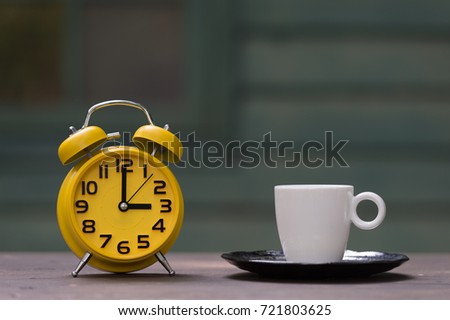 Retro alarm clock with five minutes to twelve o'clock.coffee cup on wooden table .