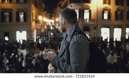 Young handsome tourist man standing in the crowd in evening. Male use the smartphone to finds direction.