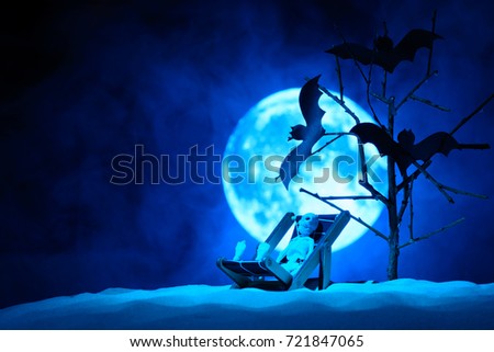 A toy skeleton on a chair to relax and three bats on a tree, the full moon in the mist behind