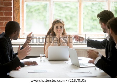 Perplexed young woman looking at coworkers pointing fingers at her. Disgruntled multiethnic team scolding female colleague who made bad work-related mistake. Stressed upset business lady in trouble.  Royalty-Free Stock Photo #721870105