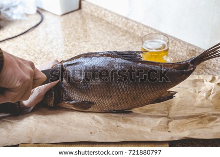 Cutting dried fish. Hands cuts a large dried-down bream with a large knife. Nearby is a mug of beer
