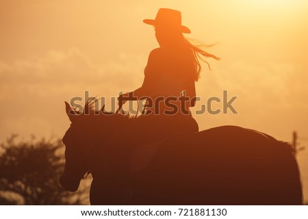 Sunset golden silhouette of young cowgirl in hat riding her horse Royalty-Free Stock Photo #721881130