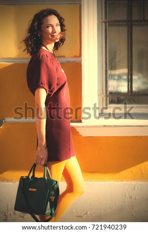 fashion. style. beautiful european woman in a burgundy dress, mustard pantyhose and with a green handbag near the old wall of the old house. instagram image filter retro style
