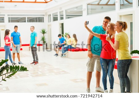 High school students on a break in the school hall, tacking pictures with smart phone 