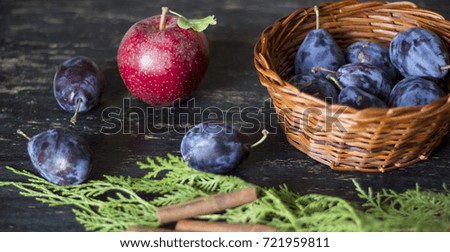 Purple organic plums, apple and autumn decoration on dark wooden table.