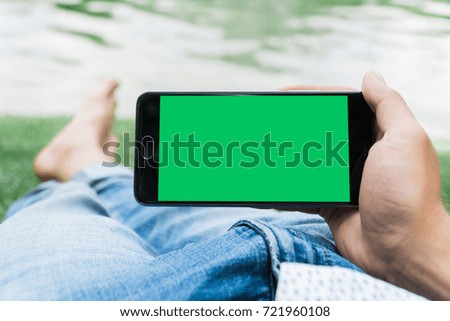 hand of man holding mobile smart phone with chroma key green screen on gren background