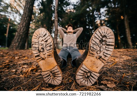 Odd weird woodcutter sitting in autumn forest on ground. Take a rest. Lunch brake on nature. Wooden sole. Wet and raw fall. Fresh air outdoor. Trees on background. Colors of seasons. Lens distortion