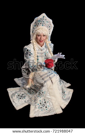 Snow Maiden in a white fur coat, kokoshnik and long hair braids gives a gift in a red box, posing on a black background