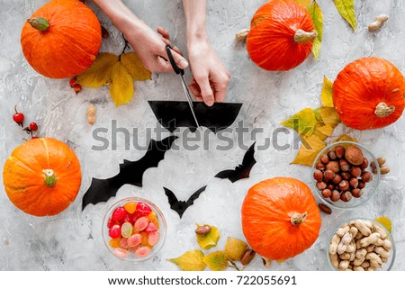 Preparing for halloween. Hands cut bats out of paper. Figures and pumpkins on grey background top view