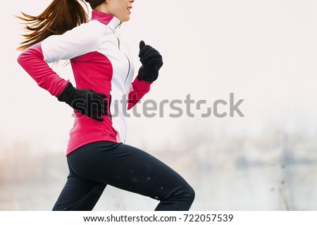 Winter running athlete woman on cold run jogging fast with speed and sprint on outside workout wearing warm clothing gloves, winter tights and wind jacket in snow weather. Royalty-Free Stock Photo #722057539