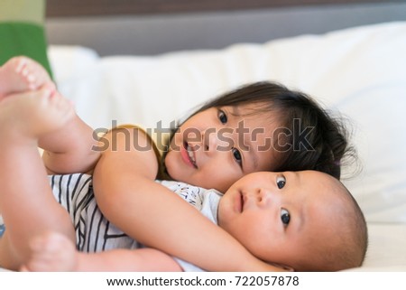 Little asian sister hugging her newborn brother and watching TV.Cute girl and new born baby boy relax in a white bedroom.Family with children at home.Love, trust and tenderness.