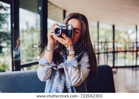 Professional female photographer making photos on vintage camera standing indoors in stylish coffee shop interior.Young woman focusing to taking pictures enjoying free time