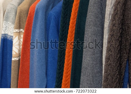 Nice warm colorful sweaters hang on hangers inside of a shopping mall. Beautiful clothes for winter autumn season. Fashion industry for men. Wool things for fall. Merchandise in a shop 