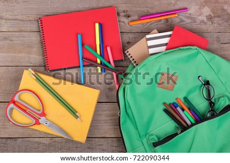 Backpack and school supplies: books, pencils, notepad, felt-tip pens, eyeglasses, scissors on brown wooden table Royalty-Free Stock Photo #722090344
