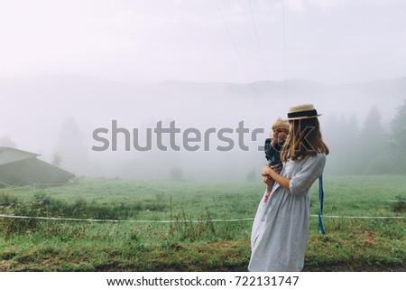 Young mother in dress holding her little baby girl and admiring the mist in the mountains