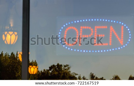 Open Sign in Storefront with reflections of Trees with Lights Illuminated in Background
