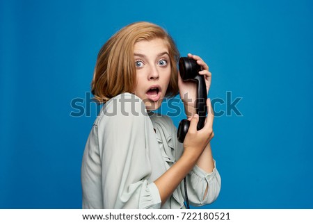 surprised, young woman holding a fixed telephone on a blue background portrait                               