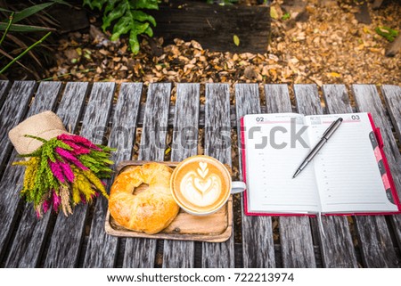 Notepads and pens Placed beside a cup of coffee and bread on a wooden table.