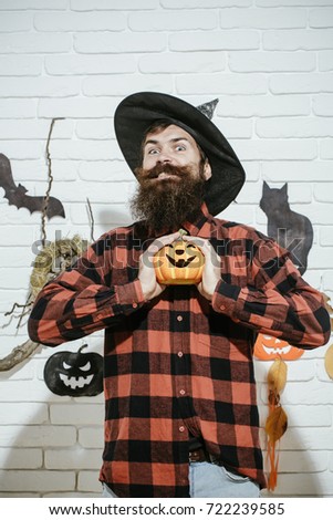Halloween man smiling pumpkin in witch hat. Happy hipster with beard in plaid shirt. Holiday celebration symbols on grey brick wall. Mystery and horror concept. Trick or treat.
