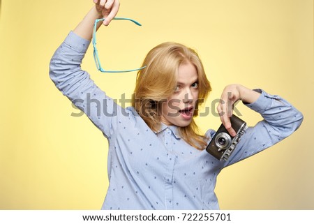 cheerful woman photographer holding transparent glasses and camera on a yellow background, pictures                               