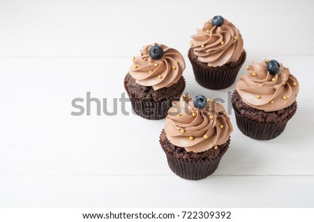 Chocolate cupcakes with whipped chocolate cream, decorated fresh blueberry, gold confectionery sprinkling on white wooden table. Picture for a menu or a confectionery catalog. Top view.