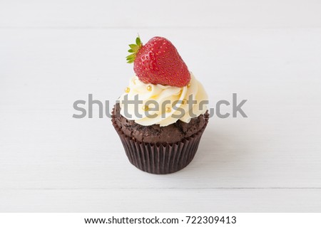 Chocolate cupcake with whipped chocolate cream, decorated fresh strawberry, gold confectionery sprinkling on white wooden table. Picture for a menu or a confectionery catalog.