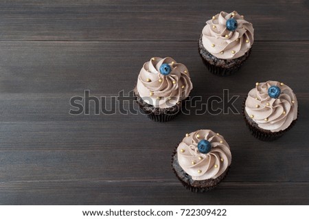 Chocolate cupcakes with whipped chocolate cream, decorated fresh blueberry, gold confectionery sprinkling on dark wooden table. Picture for a menu or a confectionery catalog. Top view.