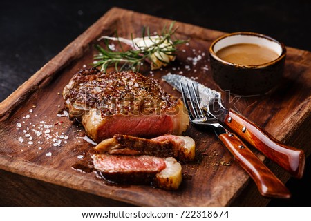 Sliced grilled meat steak New York Striploin with Pepper sauce and knife and fork on wooden board on black background Royalty-Free Stock Photo #722318674