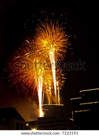 Celebration fireworks against black sky behind outline of lighted buildings