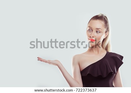 Look here. Closeup portrait happy confident young smiling woman gesturing presenting copy space at right with palm up isolated white wall background. Positive human emotion sign symbol face expression