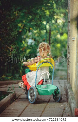 A small girl on three wheeled bicycles in the countryside. back view.