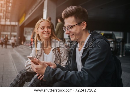 ouple or friends laughing funny and having fun with a smart phone in a big city street