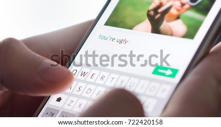 Internet troll sending mean comment to picture on an imaginary social media website with smartphone. Cyber bullying and bad behavior online concept. Royalty-Free Stock Photo #722420158