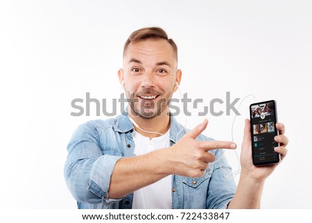 Cheerful young man pointing at phone with music player
