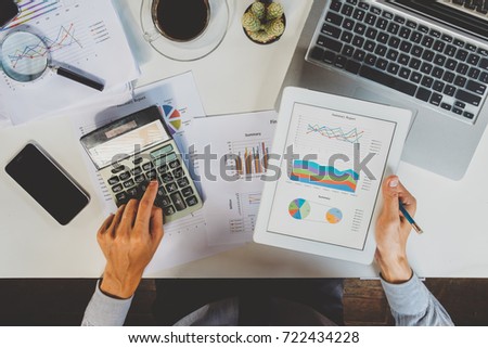 Businessman working with digital tablet and calculator and document on wooden desk in modern office.Business analysis and strategy concept.