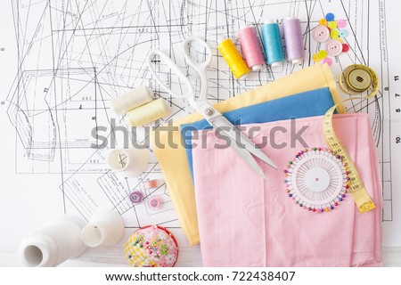 Sewing supplies on a white wooden table: sewing thread, scissors, a large spool of thread, pieces of cloth, needles,centimeter, buttons Royalty-Free Stock Photo #722438407