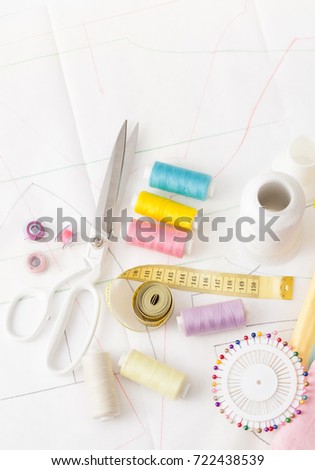 Sewing supplies on a white wooden table: sewing thread, scissors, a large spool of thread, pieces of cloth, needles,centimeter, buttons