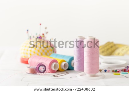 Sewing supplies on a white wooden table: sewing thread, scissors, a large spool of thread, pieces of cloth, needles,centimeter, buttons Royalty-Free Stock Photo #722438632