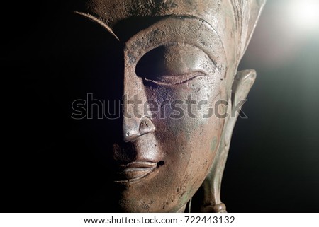 Spiritual enlightenment. Buddha head with divine light. Bronze statue face in close up against black background with copy space.