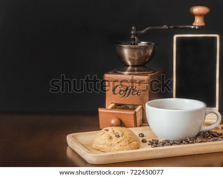 White cup coffee and cookie on wooden tray with coffee grinder and blank chalk board on wooden top table 