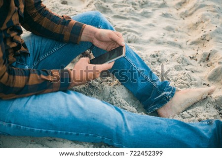 Closeup on person using mobile smartphone over sandy beach background. Photography concept for online connection, communication messaging, banking..