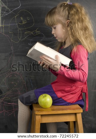 portrait of cute little girl with book and green apple near blackboard