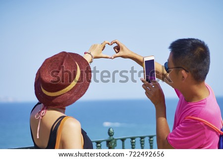 Asian couple making a heart shape toward ocean with hands 